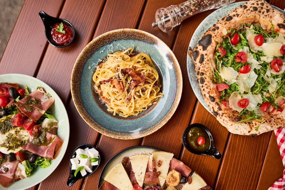 Pasta carbonara, pizza and salads on a wooden table